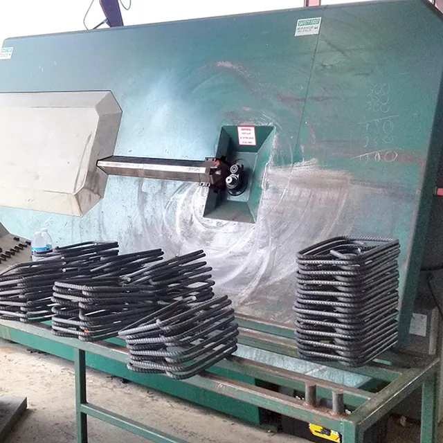 A stirrup bender with stacks of finished rebar stirrups on the rack in front of it.