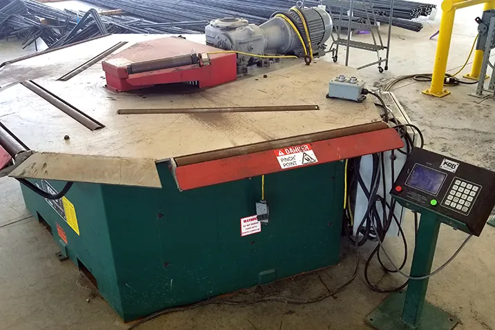 A KRB machine with a steel work table, a top-mounted motor and gearbox, and a keypad control pedestal.